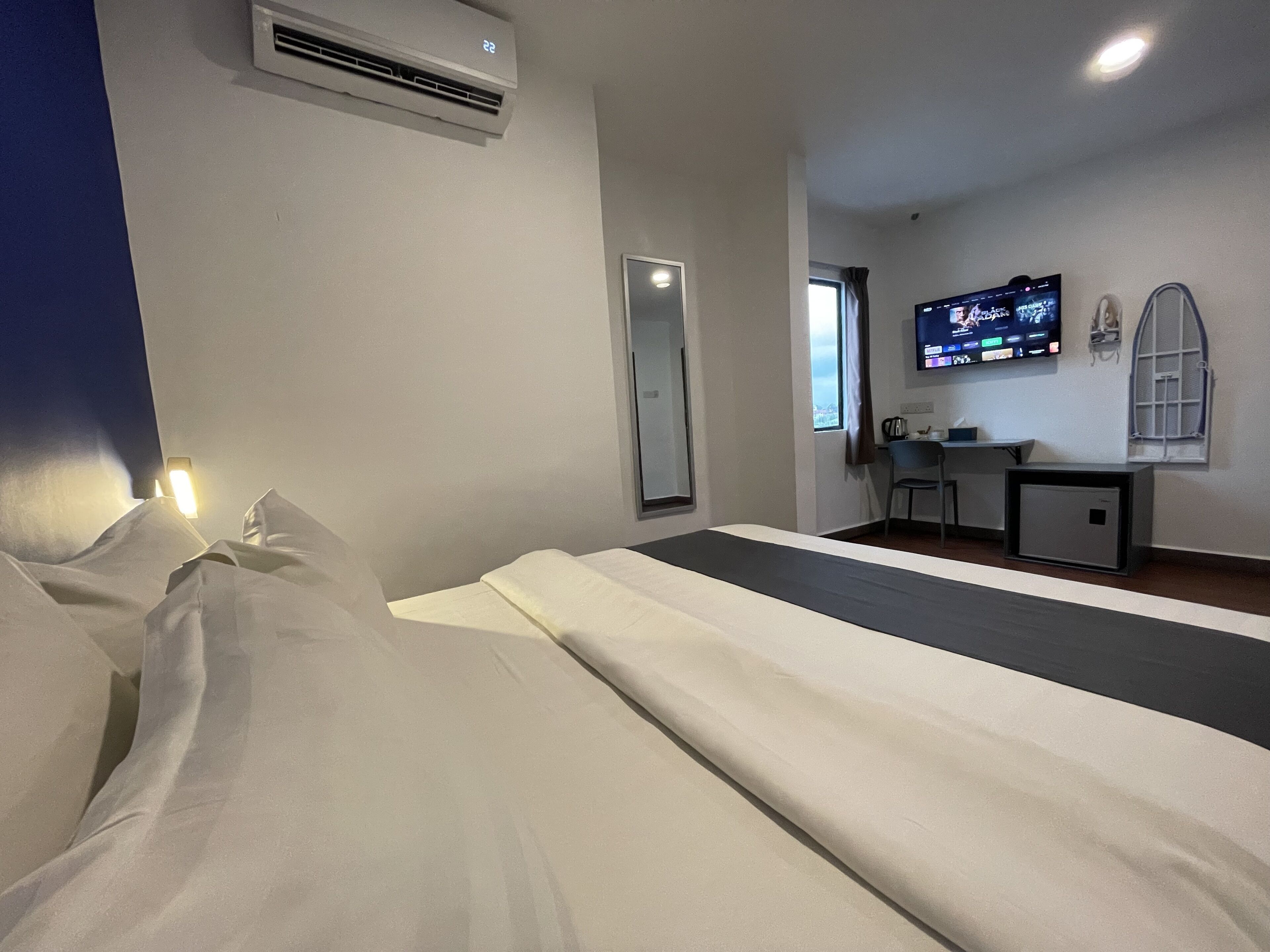 Een hotelkamer met een bed, bureau, televisie en airconditioning.