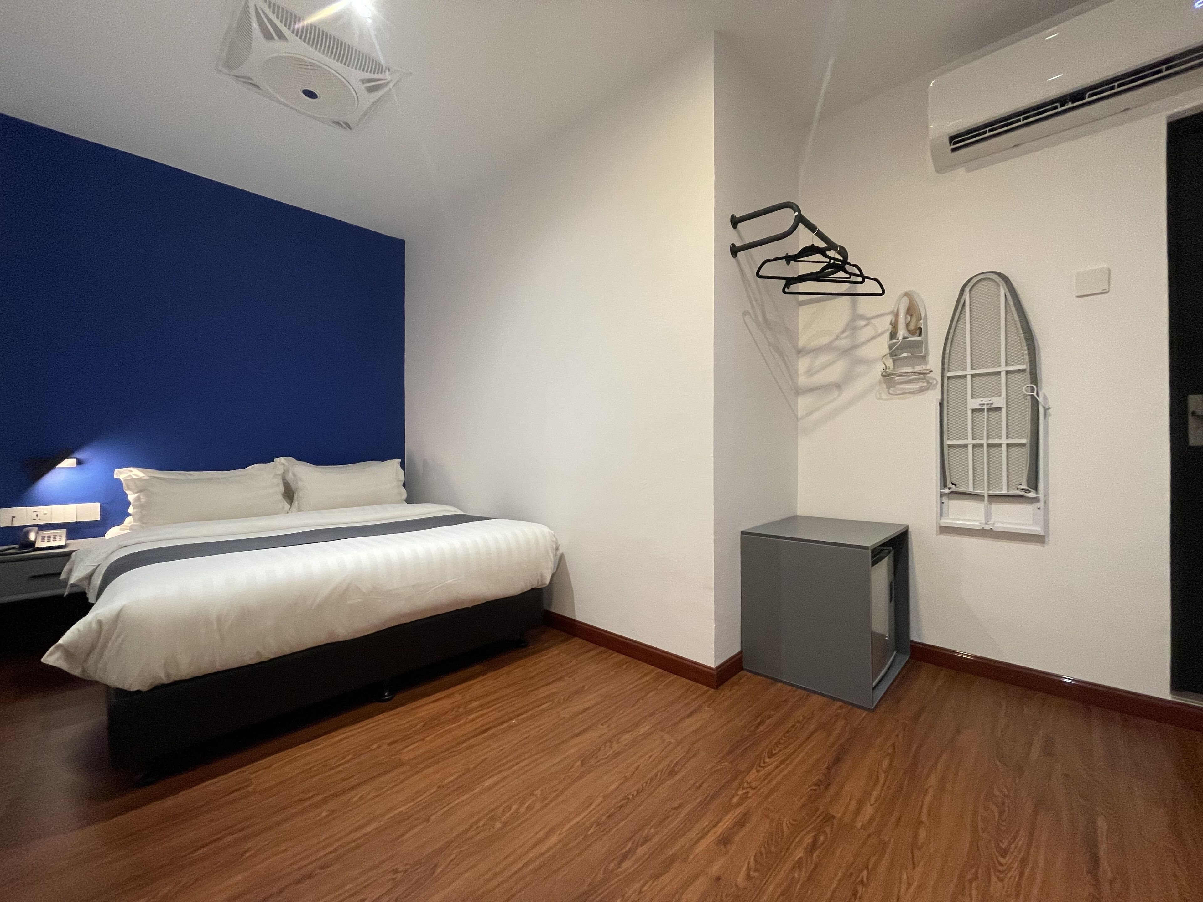 A modern hotel room with a bed, a small bedside table, a wall-mounted heater, a window with a view, and a door.