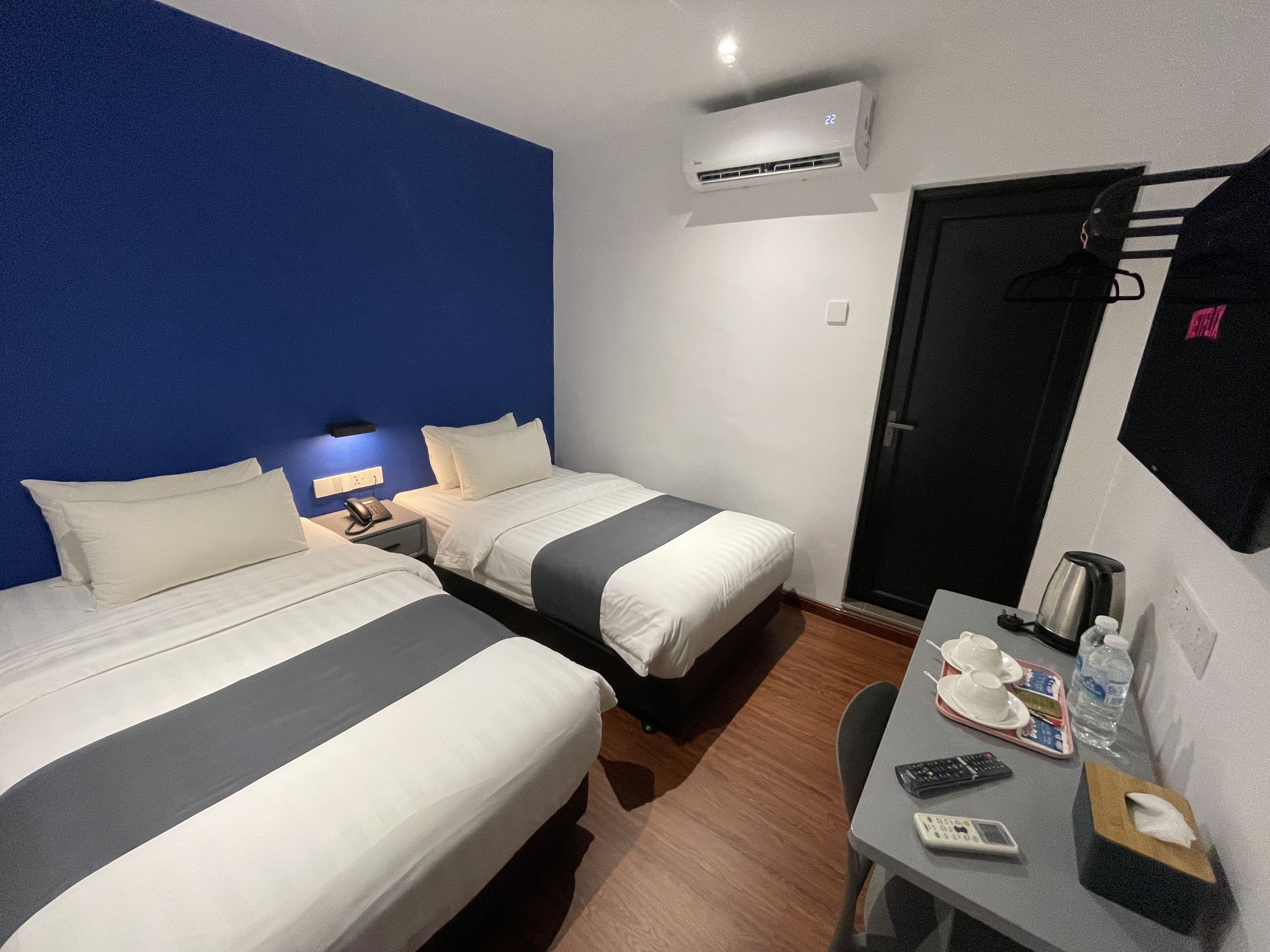 A hotel room with two beds, a desk with a chair, a coffee maker, a phone, and a door.