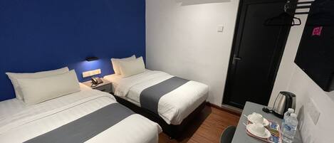 A hotel room with two beds, a desk with a chair, a coffee maker, a phone, and a door.