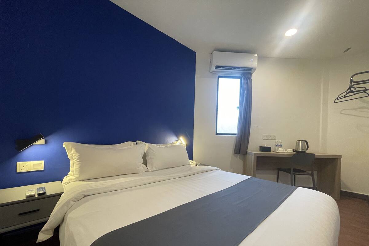 Une chambre d’hôtel avec un lit, une table de chevet, une lampe et une fenêtre avec des rideaux.
