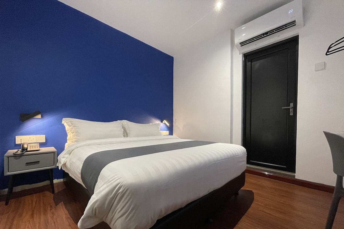 Une chambre d’hôtel moderne avec un grand lit, une table de chevet avec un téléphone et une porte sombre.
