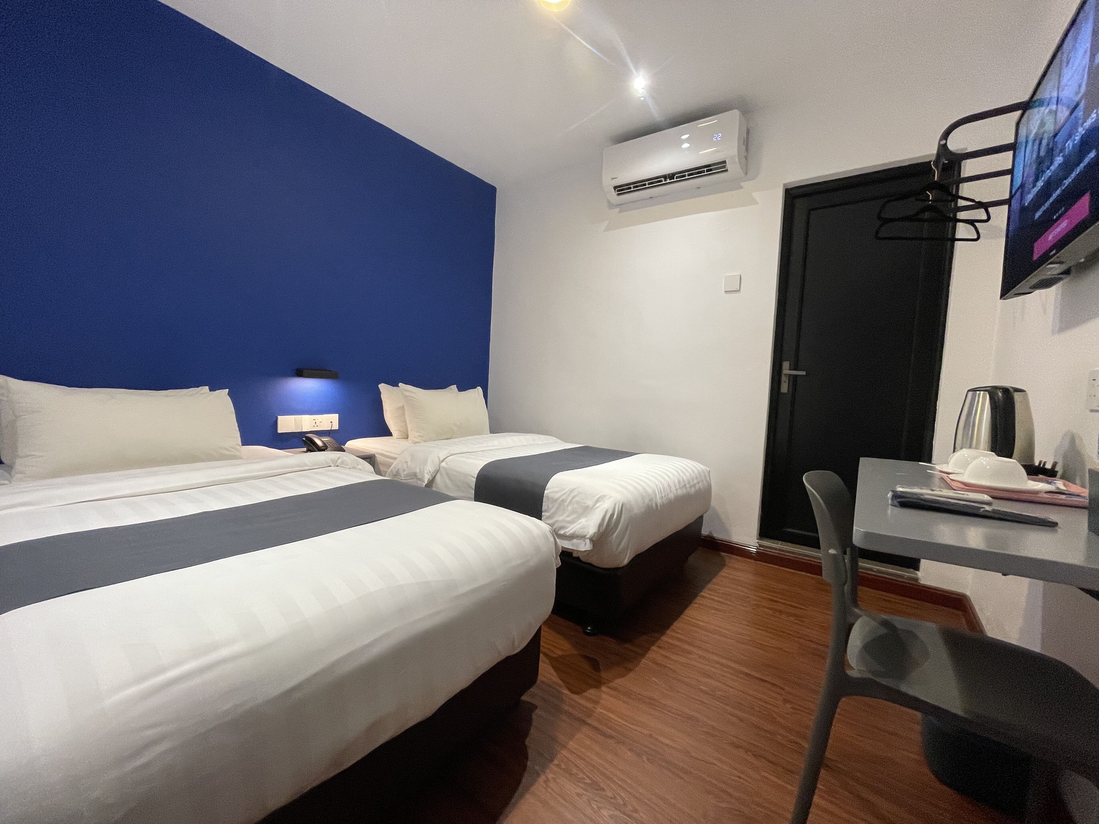 A hotel room with two beds, a desk, a chair, an air conditioning unit, and a TV mounted on the wall.