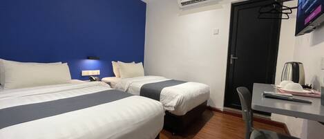 A hotel room with two beds, a desk, a chair, an air conditioning unit, and a TV mounted on the wall.