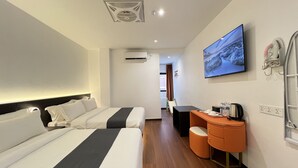 Quarto de hotel com duas camas, televisão, aparelho de ar condicionado, uma mesinha com chaleira e banheiro com porta-toalhas.