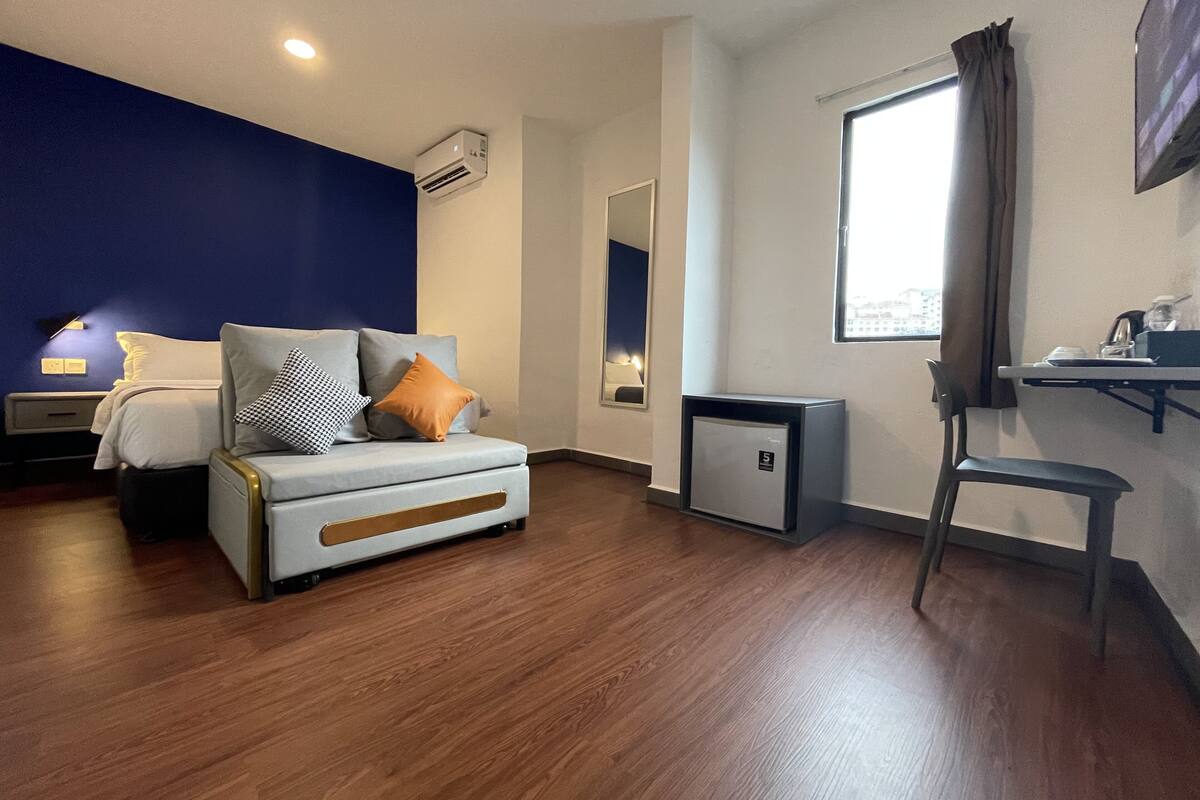 Une chambre d’hôtel moderne équipée d’un lit, d’un bureau, d’une chaise et d’un petit réfrigérateur.