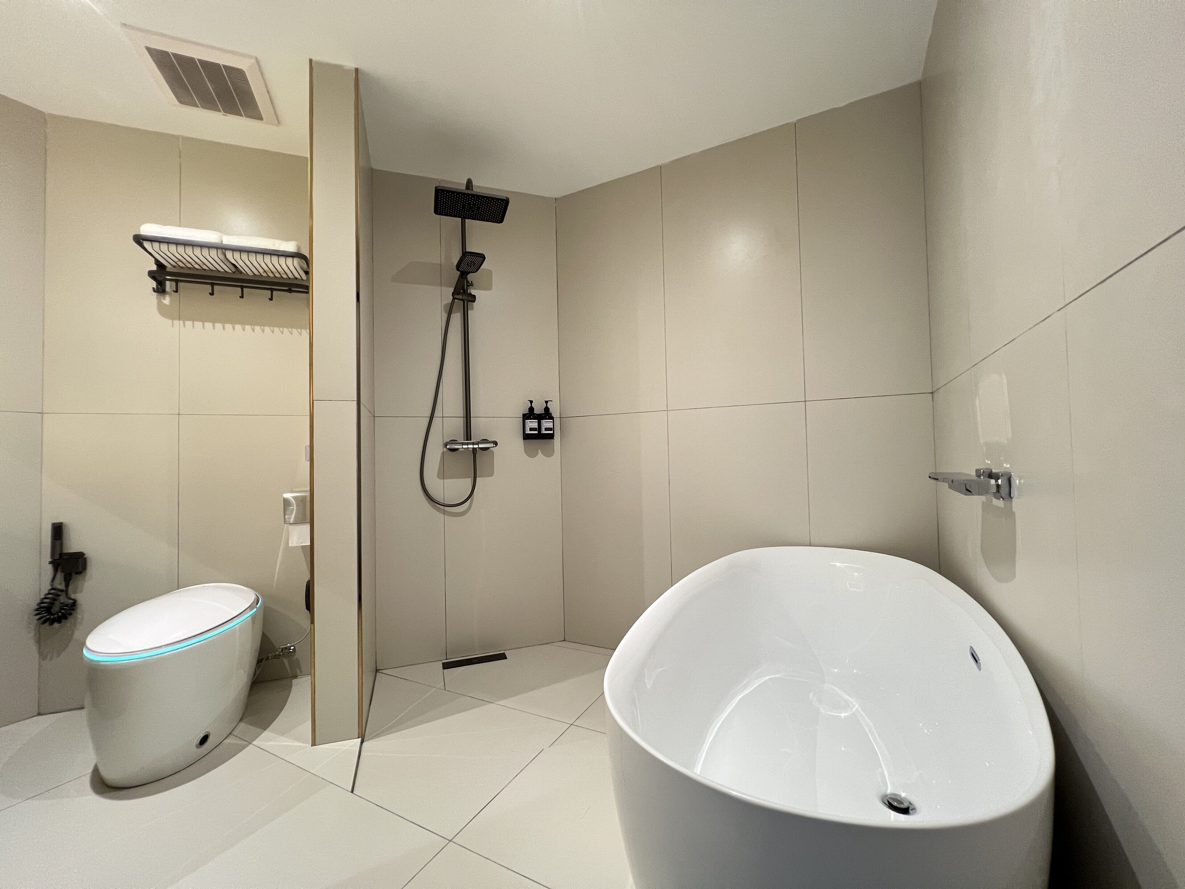 Un baño moderno con inodoro blanco, una bañera grande y una zona de ducha.