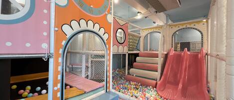 Espaço de recreação infantil com escorrega, piscina de bolinhas e estruturas de jogo fechadas.