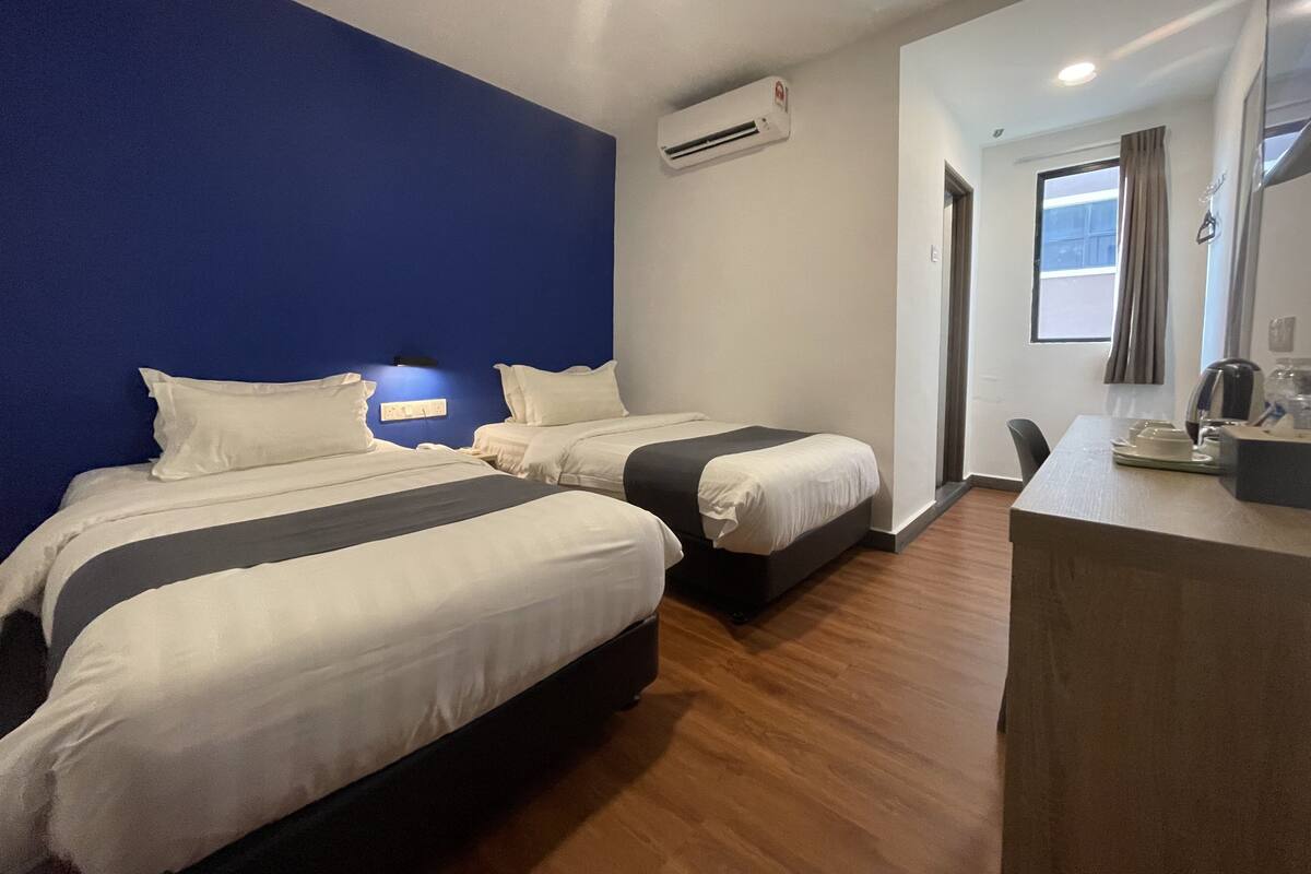 Une chambre d’hôtel avec deux lits, un bureau avec une chaise, un appareil de climatisation et une fenêtre avec des rideaux.