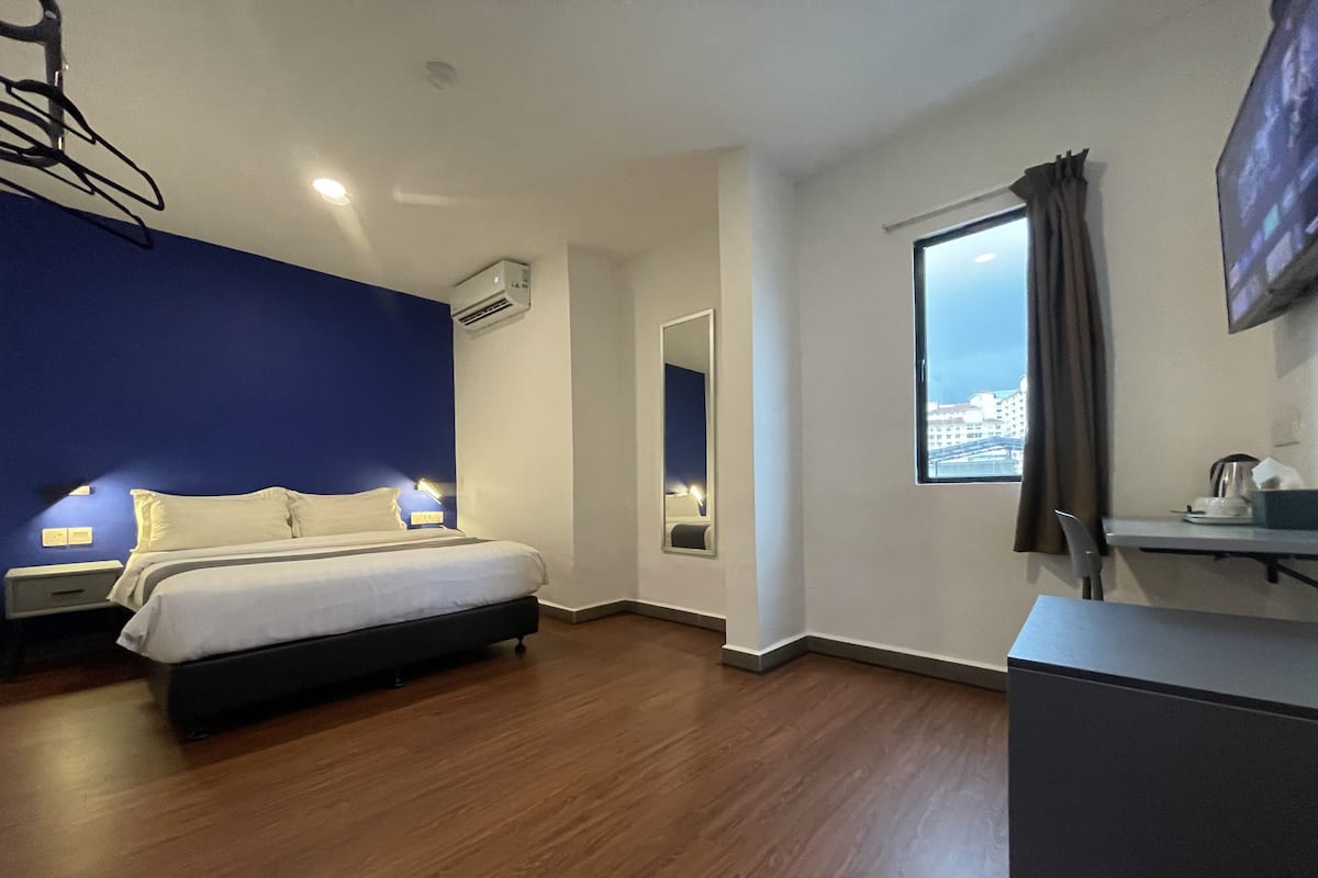 Une chambre à coucher comprenant un lit, des lampes de chevet, une fenêtre avec des rideaux, un appareil de climatisation et une vue sur les bâtiments environnants.