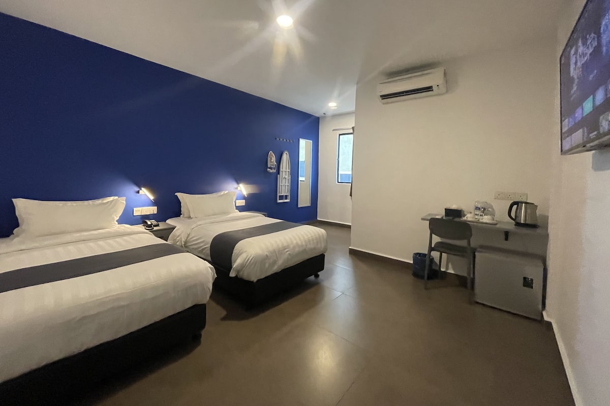 Une chambre d’hôtel avec deux lits, un bureau, une chaise, un climatiseur et une fenêtre.