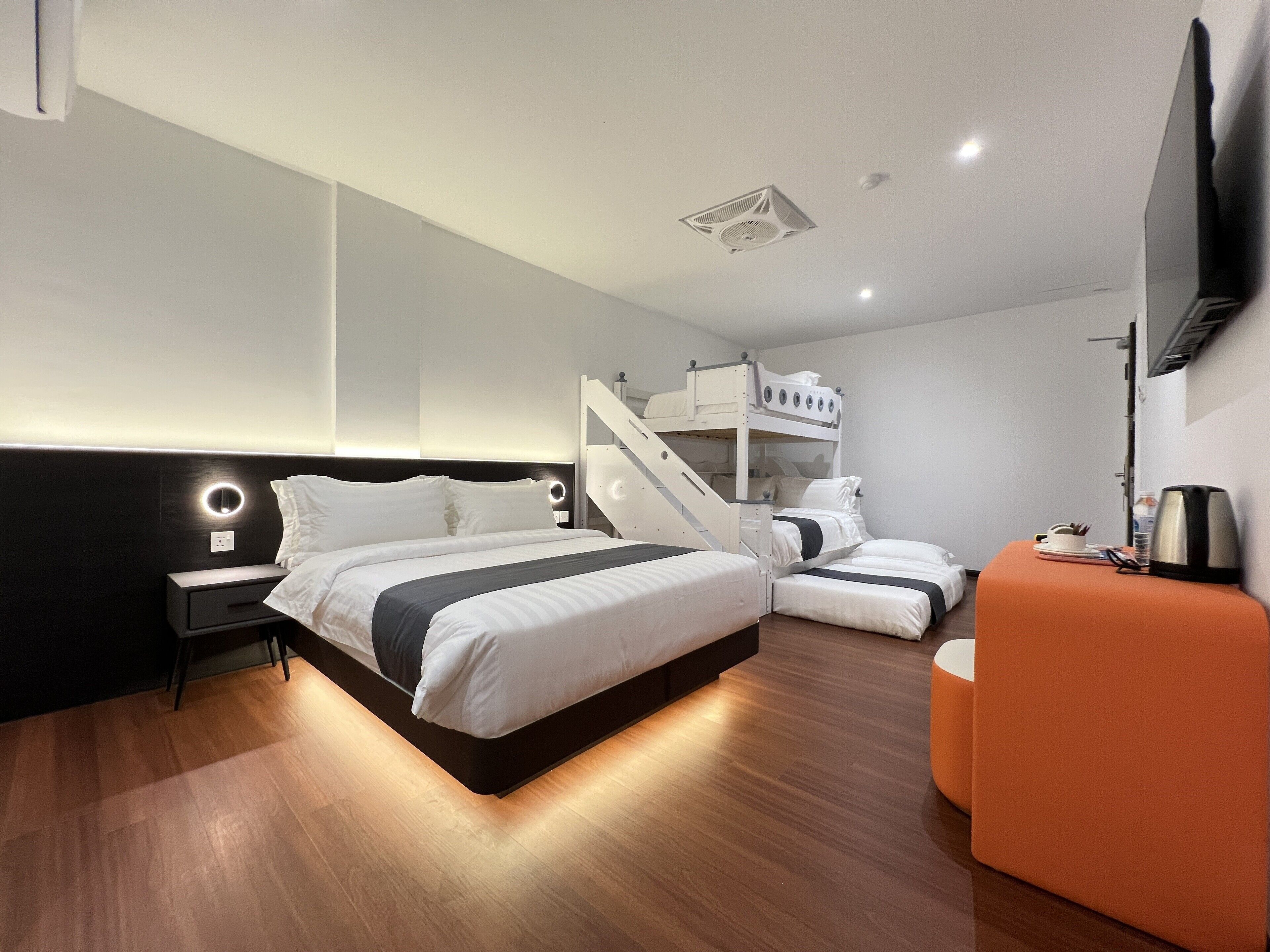 Una habitación de hotel moderna con una cama grande, un pequeño rincón de descanso y una escalera que sube a una litera superior.
