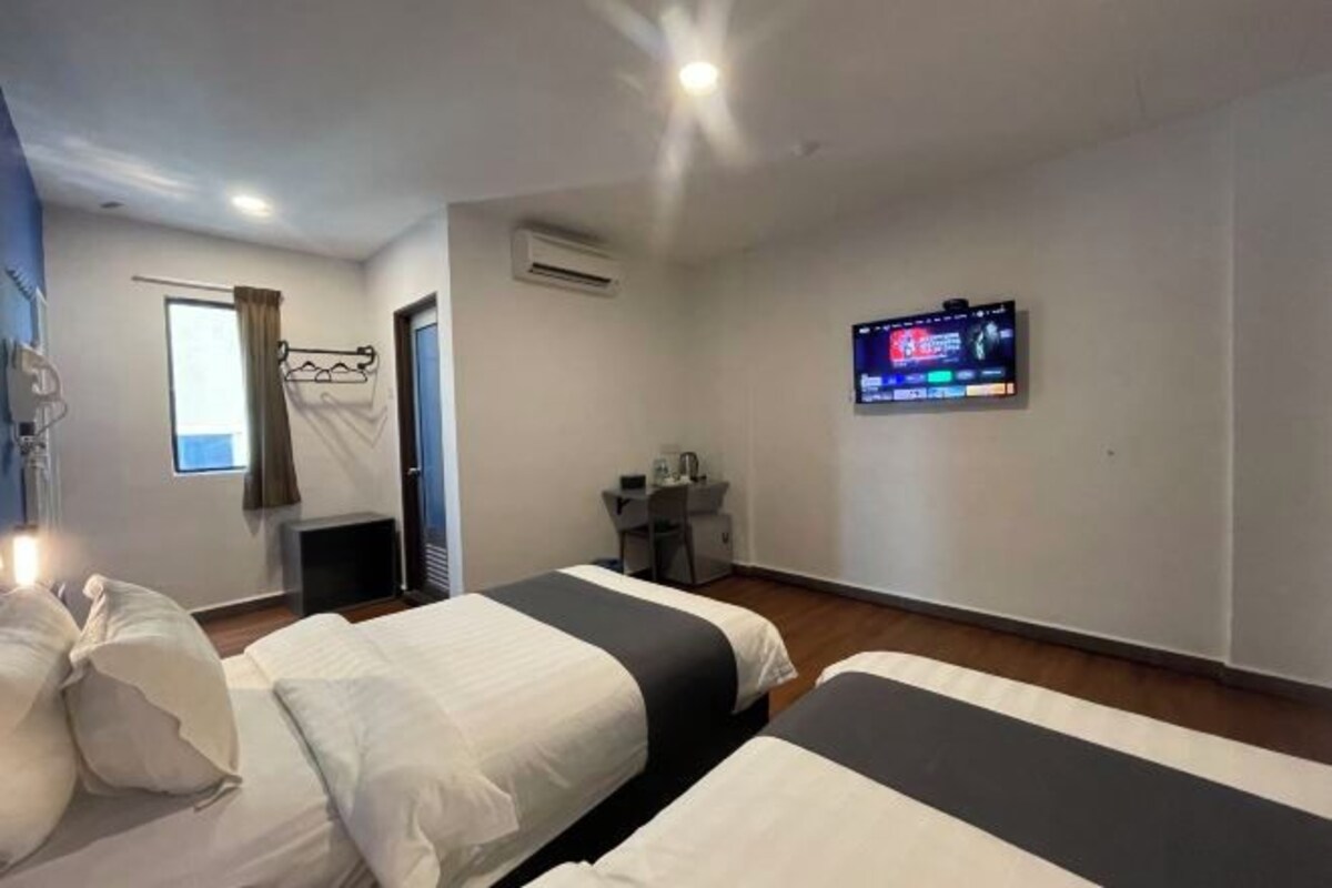 Una habitación de hotel con dos camas, un escritorio, una silla, un televisor y una ventana con cortinas.