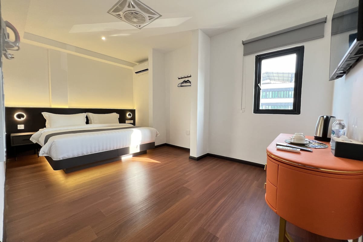 Une chambre d’hôtel moderne avec un grand lit, une petite table d’appoint orange et une fenêtre donnant sur des immeubles.
