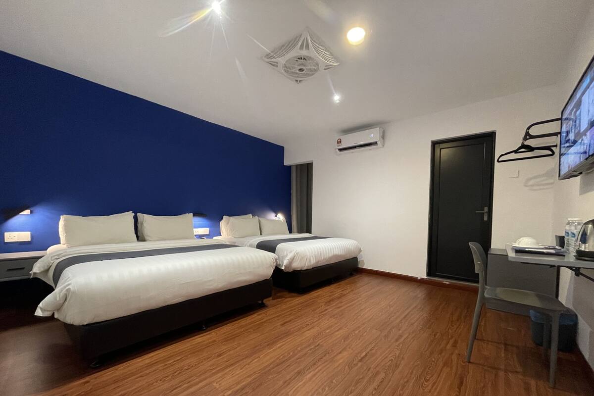 Une chambre d’hôtel avec deux lits, un bureau, une chaise et un téléviseur fixé au mur.