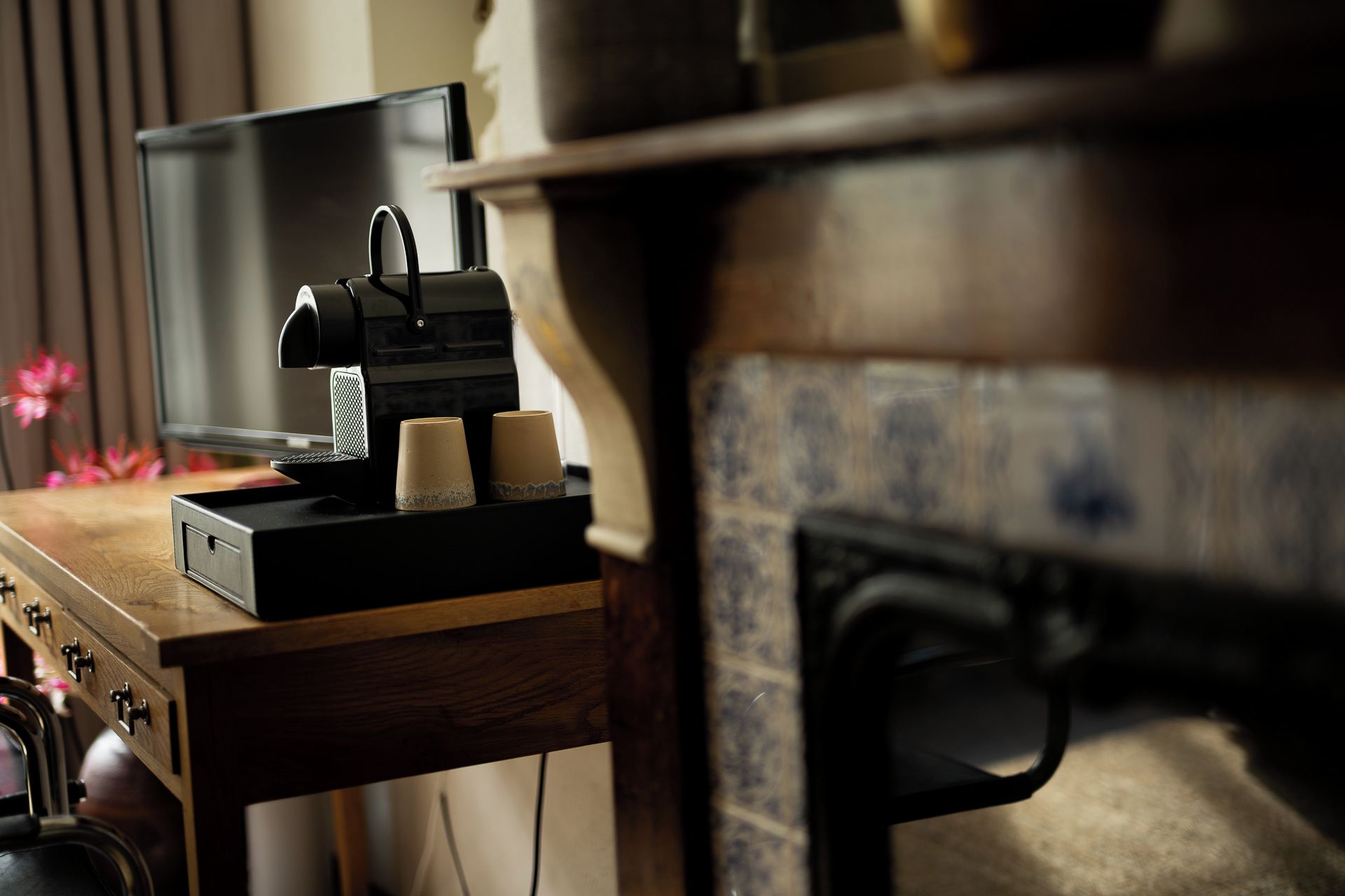 A coffee machine on a wooden table with two paper cups, a television, and a fireplace in the background.