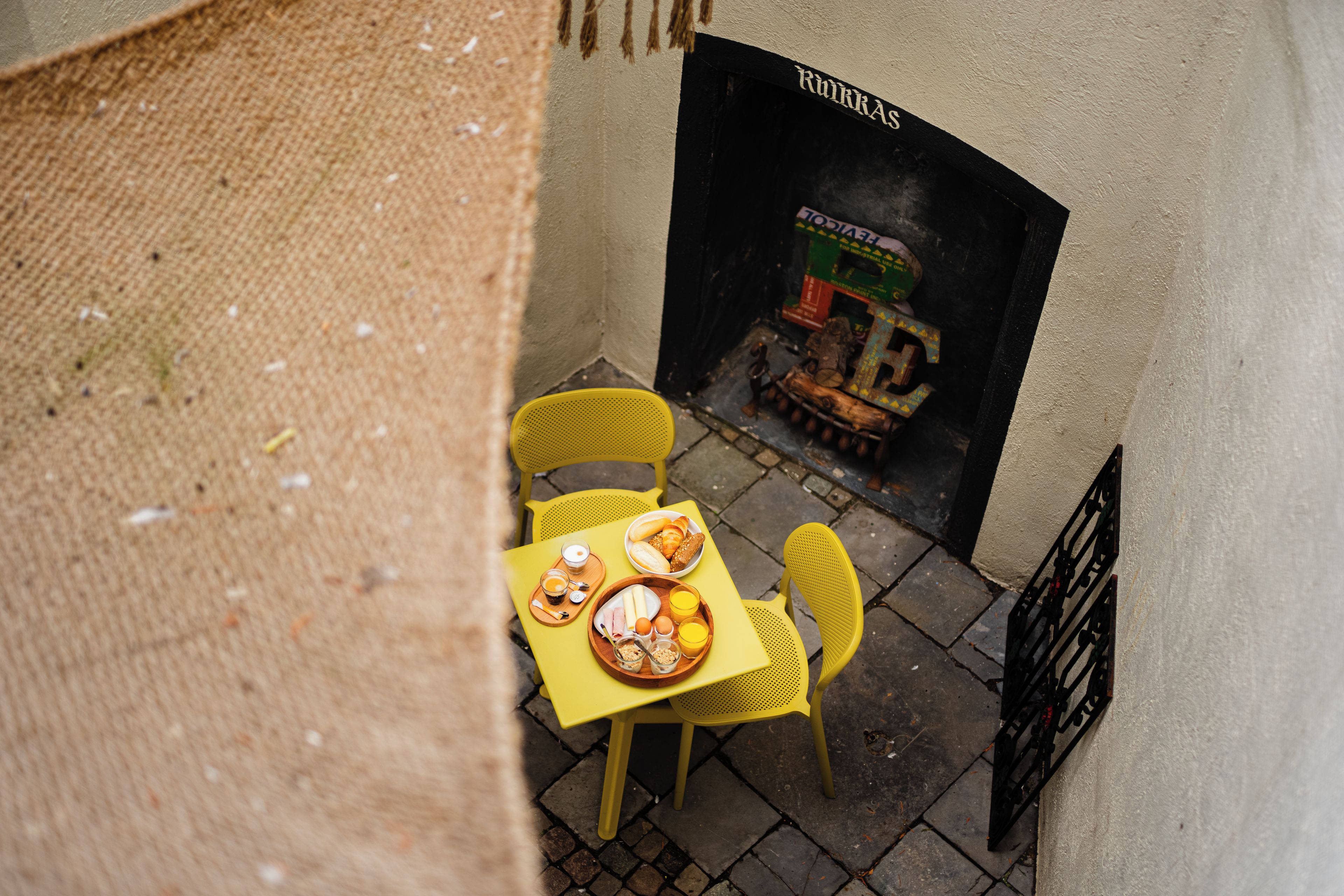 A yellow table with breakfast items and a yellow chair, a black metal gate, and a building with a sign reading 'RuhrAS'.