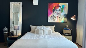 A bedroom with a bed, pillows, a nightstand, a lamp, a painting, and a vintage radio. - Boutique Hotel BE41 (Maastricht)