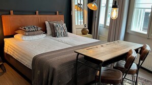 A hotel room with a bed, a wooden table, two chairs, a nightstand, and a window with curtains. - Boutique Hotel BE41 (Maastricht)