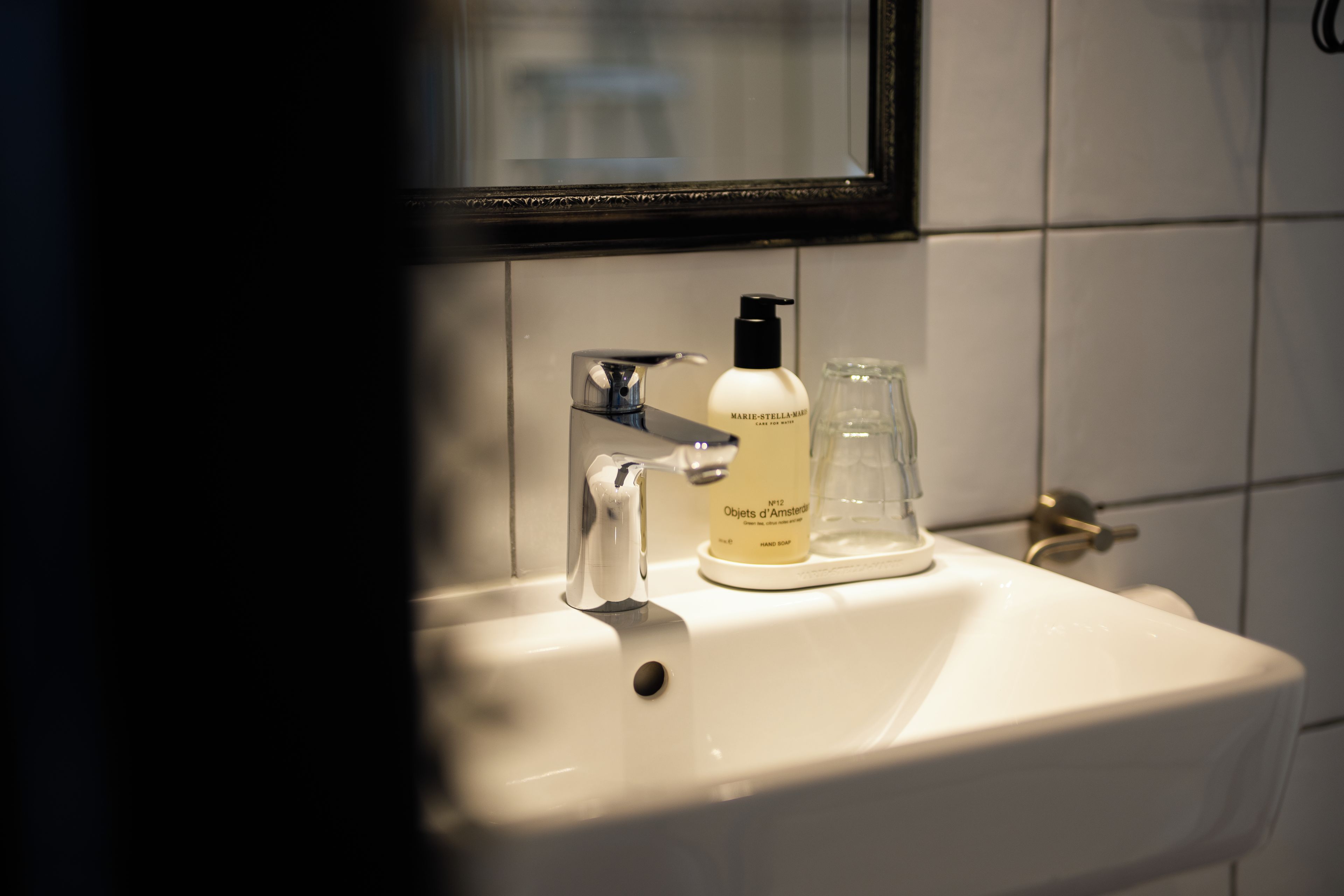 A bathroom sink with a hand soap bottle and a glass.