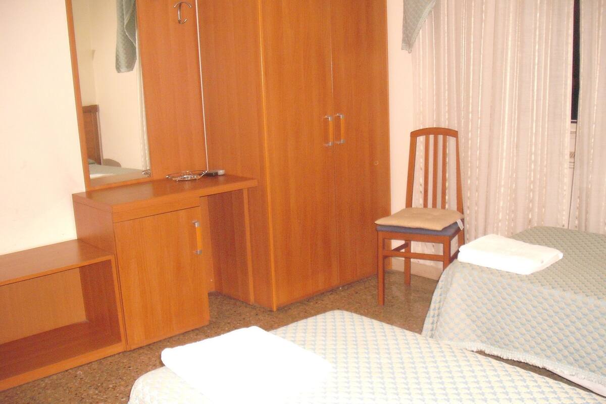 Un dormitorio con un armario de madera, una silla y dos camas con ropa de cama estampada.