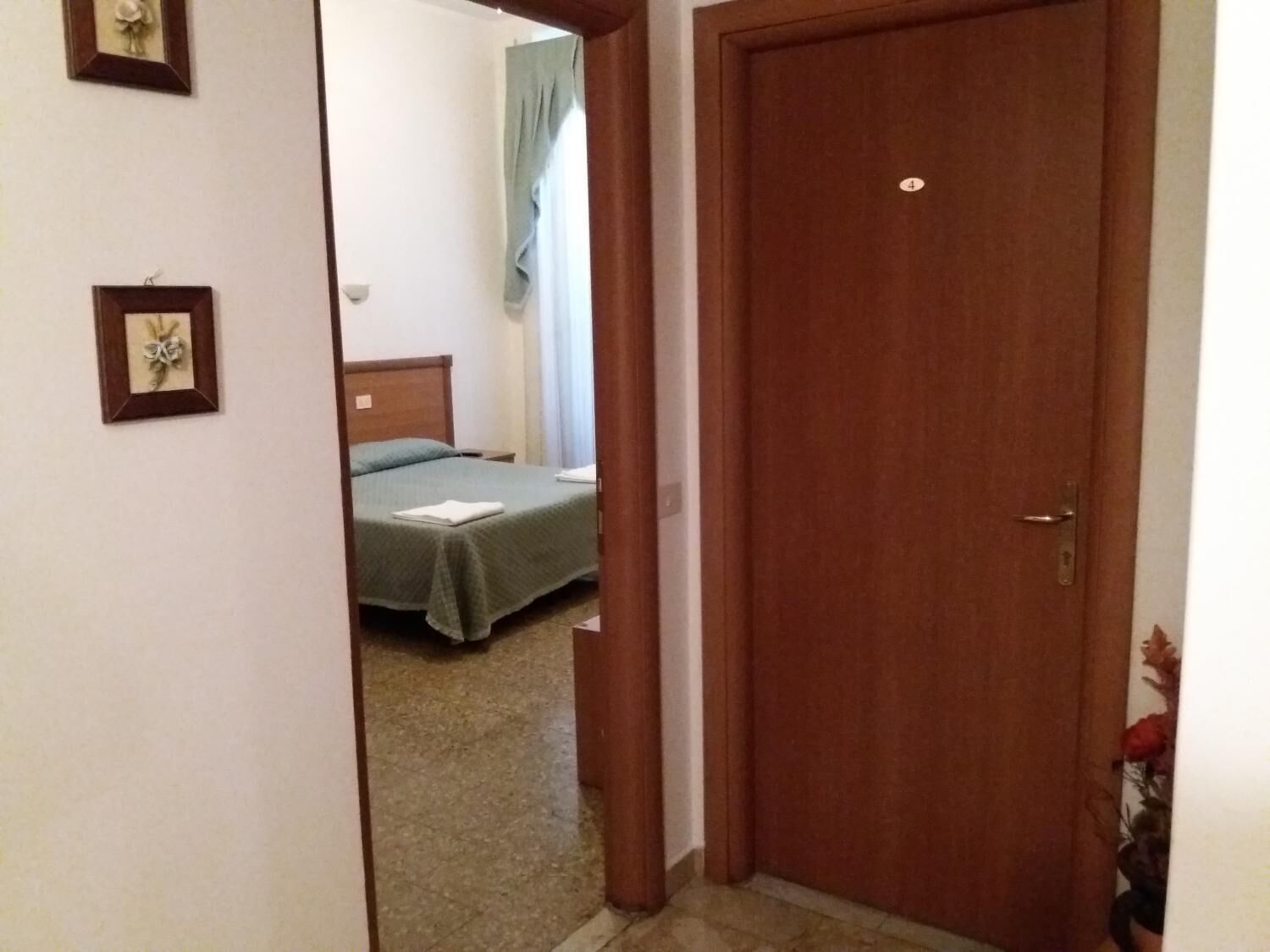 A hotel room with a wooden door, a bed with a green bedspread, and a nightstand.