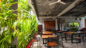 A restaurant with indoor plants, wooden tables, and black chairs. - Joe Fisherman Inn (Pangkor Island)