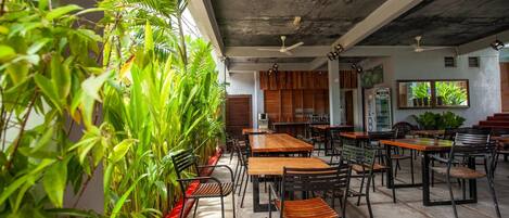 Un restaurant décoré de plantes d’intérieur, avec des tables en bois et des chaises noires.