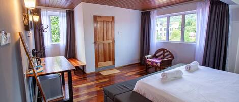 A hotel room with a wooden ceiling, a bed with white linens, a desk with a chair, and a window with curtains.