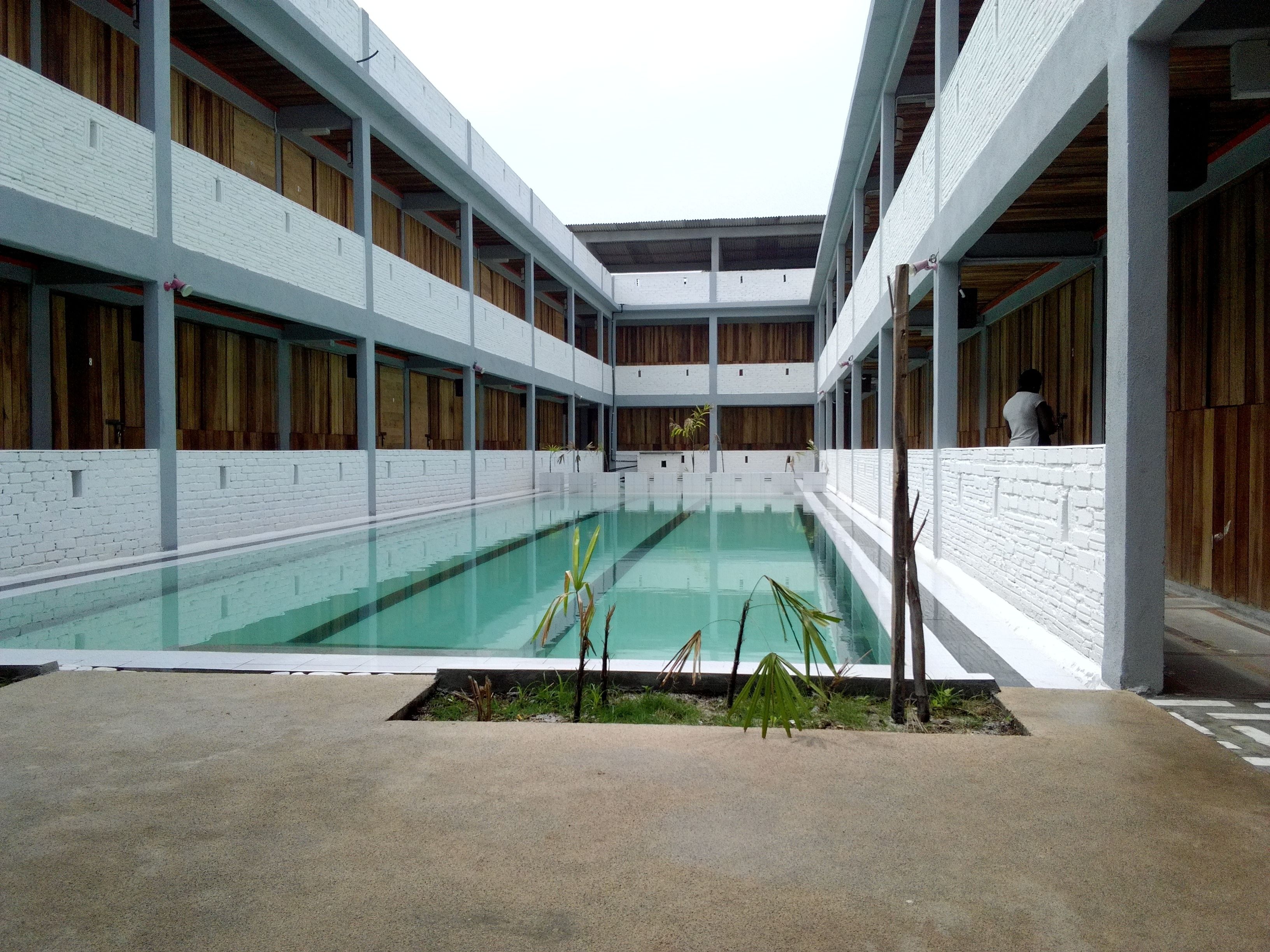 A modern building with a central swimming pool, surrounded by white brick walls and wooden paneling.