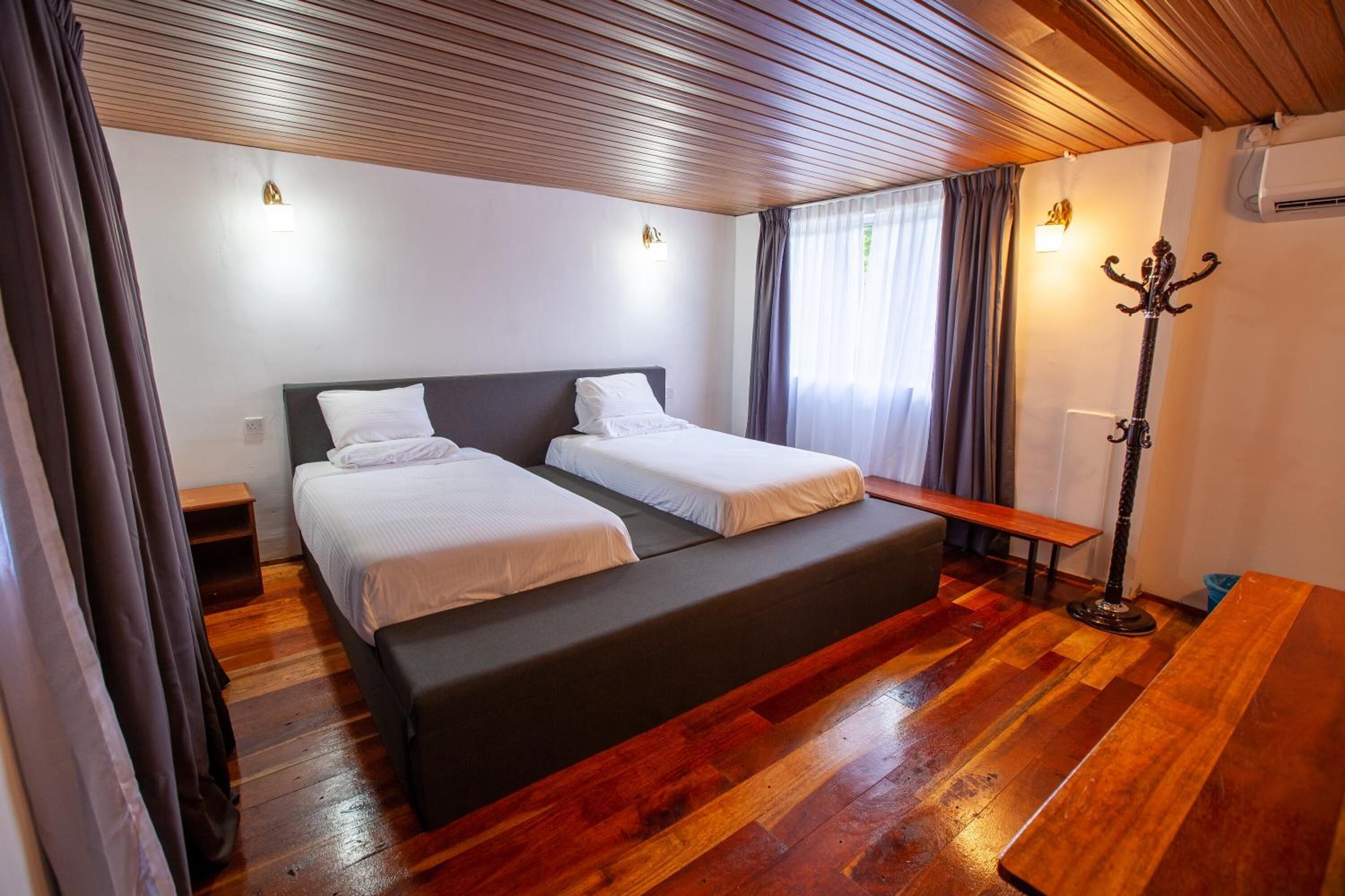 Una habitación con una cama grande, un banco, un perchero y suelo de madera.