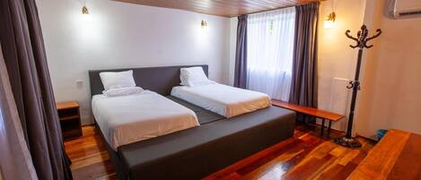 Una habitación con una cama grande, un banco, un perchero y suelo de madera.