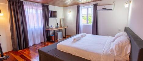 A hotel room with a wooden ceiling, a bed with white linens, a desk with a computer, and a window with curtains.
