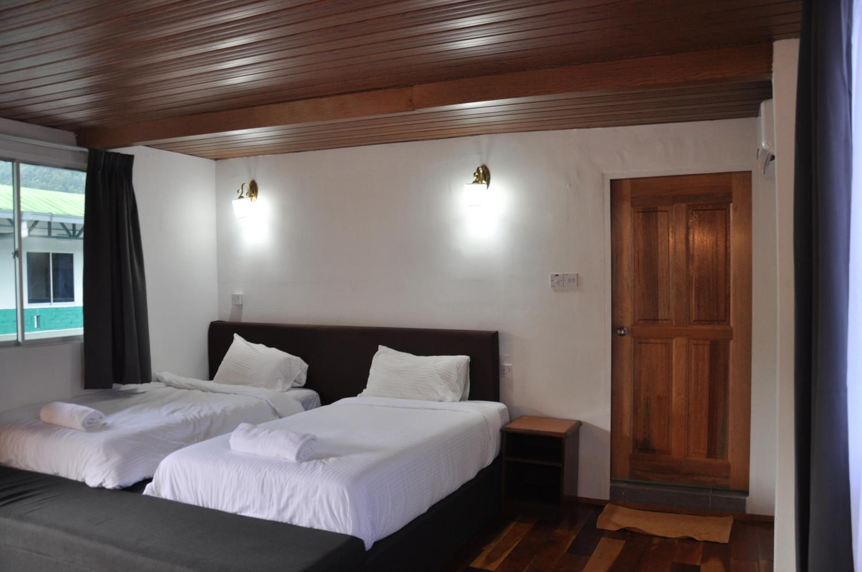A hotel room with two beds, wooden ceiling, a wooden door, and a window with curtains.