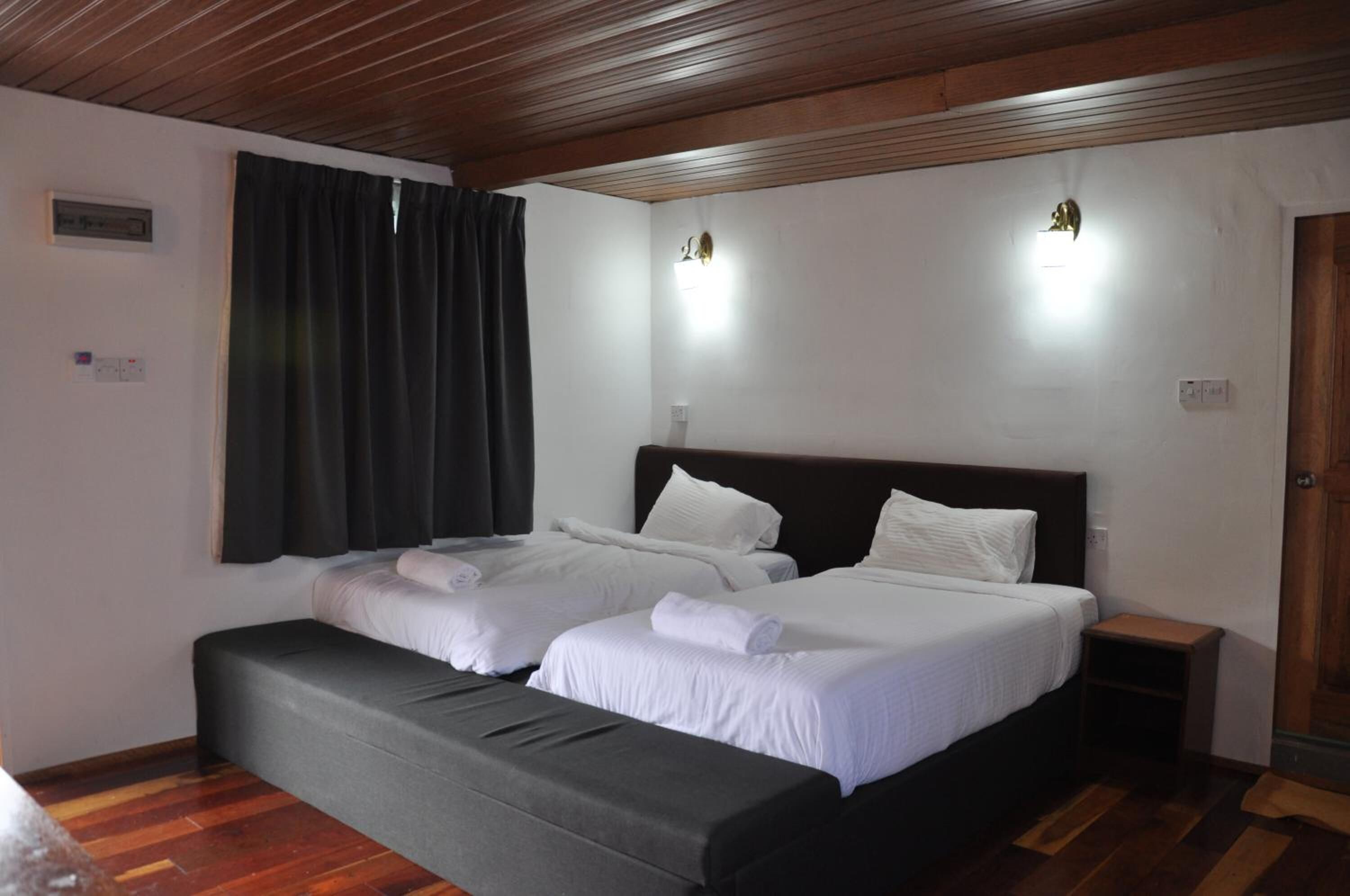 Een hotelkamer met twee bedden, een bankje, een tafeltje en een houten plafond.