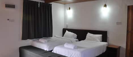 A hotel room with two beds, a bench, a small table, and a wooden ceiling.