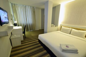 Et hotelværelse med seng, skrivebord, fjernsyn og bruseområde.