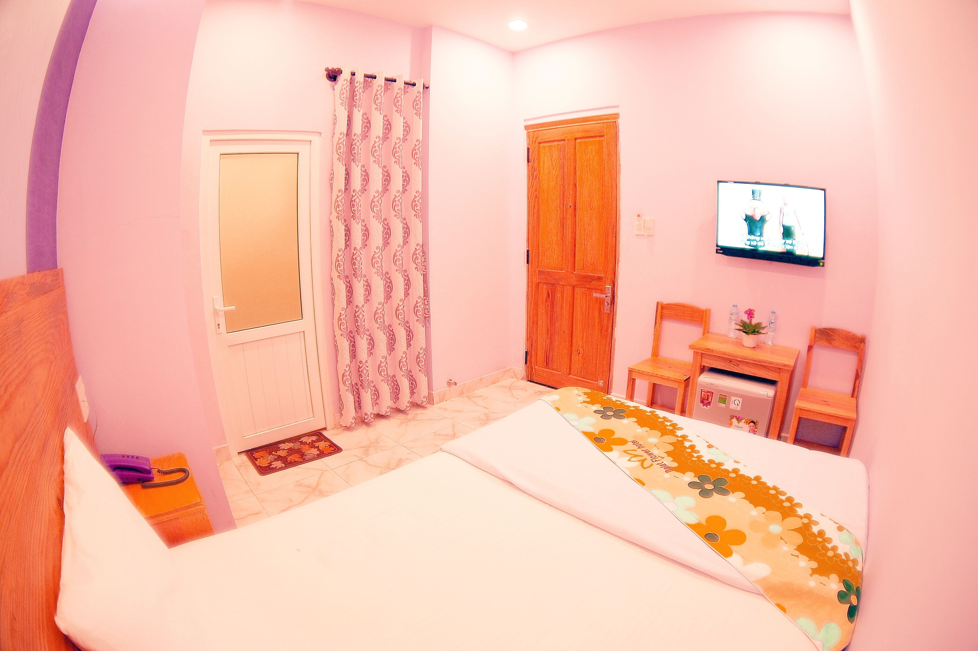 A bedroom with a bed, a wooden door, a television, and a small desk with a chair.