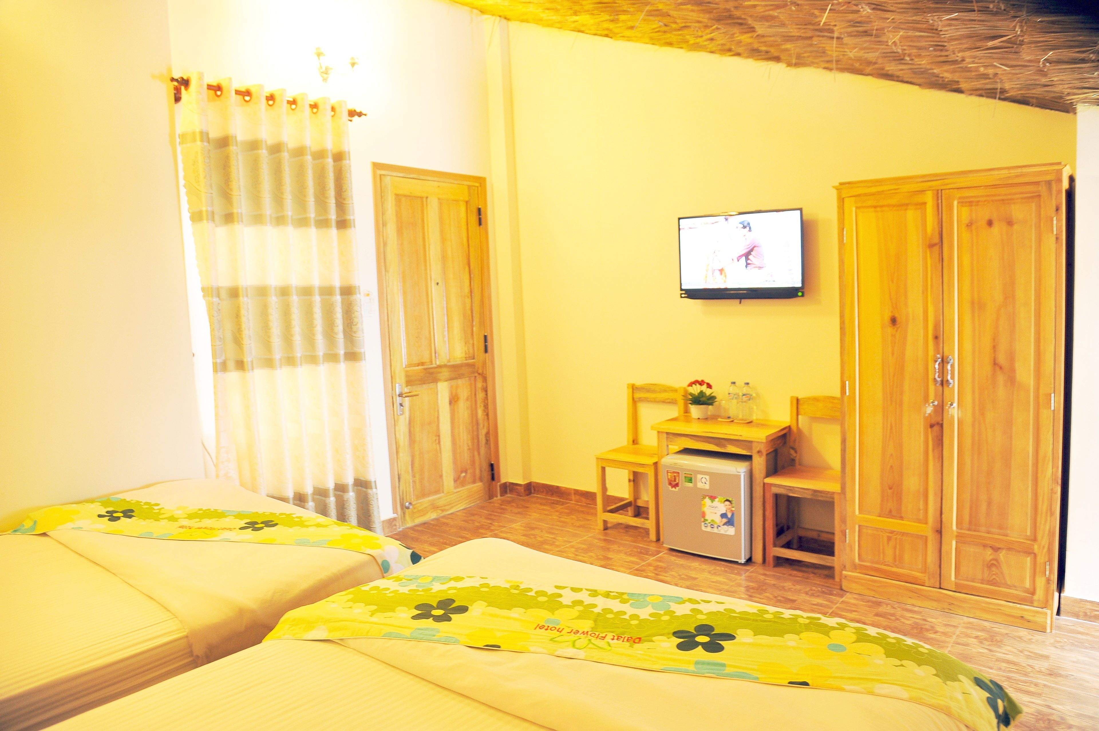 A room with two beds, a TV on the wall, wooden furniture, and a small table with a plant.