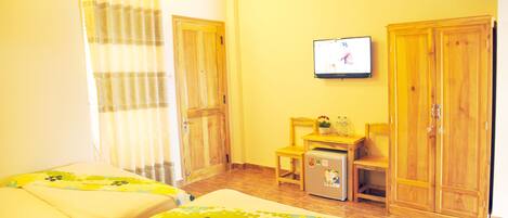 A room with two beds, a TV on the wall, wooden furniture, and a small table with a plant.