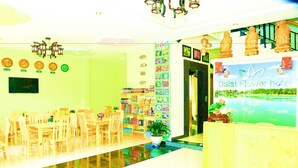A hotel lobby with a reception desk, a wall clock, and a seating area with wooden chairs and tables.