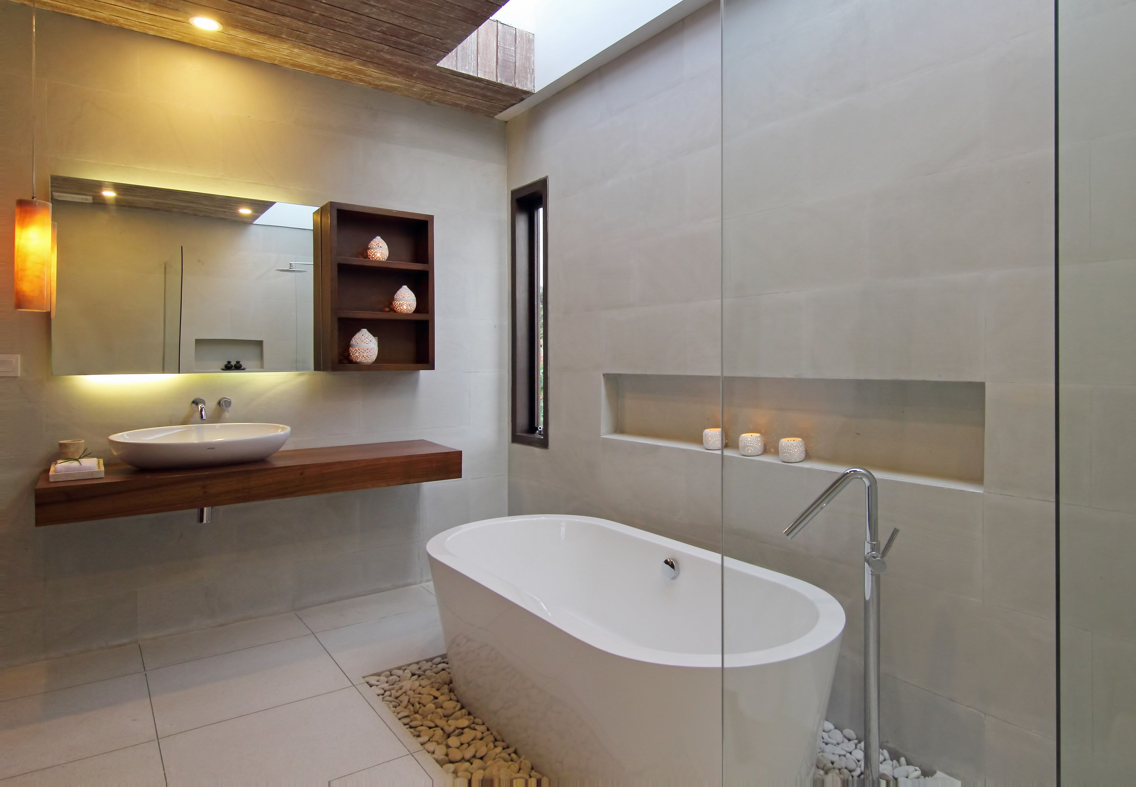 A modern bathroom with a freestanding bathtub, a large mirror, and a wooden shelf with decorative items.