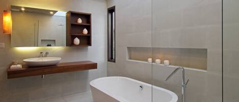 A modern bathroom with a freestanding bathtub, a large mirror, and a wooden shelf with decorative items.