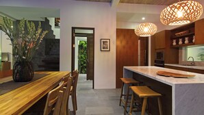 A modern kitchen with a wooden island, bar stools, and pendant lighting. - AbivillA Seminyak (Seminyak)