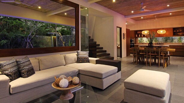A modern living room with a large sectional sofa, a glass coffee table, and a dining area with wooden chairs and a kitchen in the background. - AbivillA Seminyak (Seminyak)
