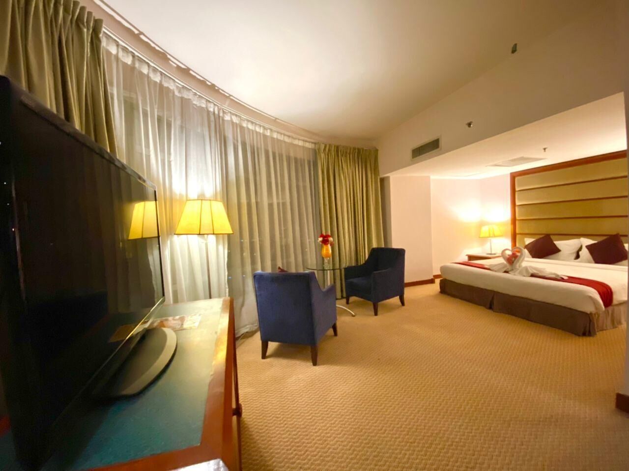 Een hotelkamer met een bed, twee fauteuils, een televisie en een lamp.
