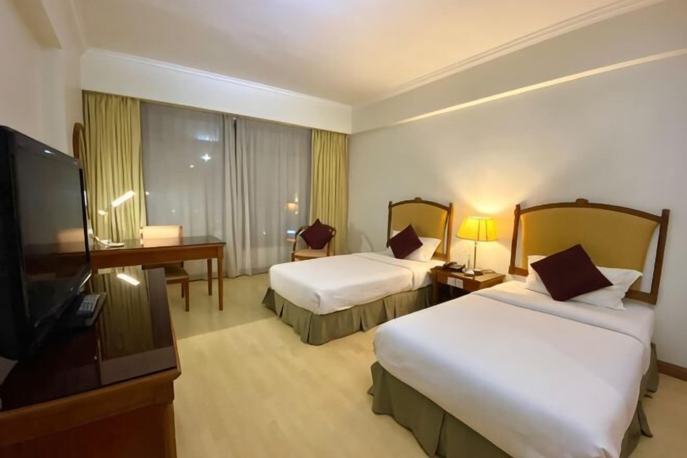 Habitación de hotel con dos camas, un escritorio con televisor y un ventanal con cortinas.
