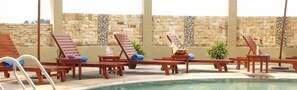 A poolside area with wooden lounge chairs and tables, a stone wall in the background, and a clear pool. - Oriental Crystal Hotel Kajang (Kajang)