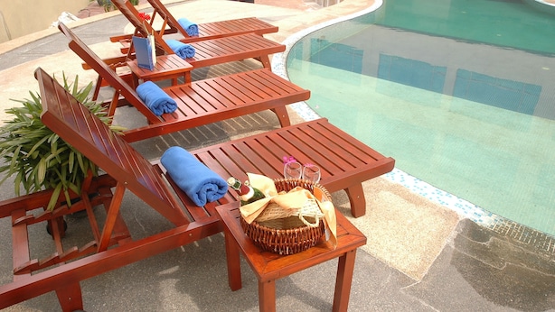 A poolside area with wooden lounge chairs, a small table with a basket containing a bottle and glasses, and potted plants. - Oriental Crystal Hotel Kajang (Kajang)