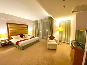 A hotel room with a large bed, a chair, a desk, and a television.